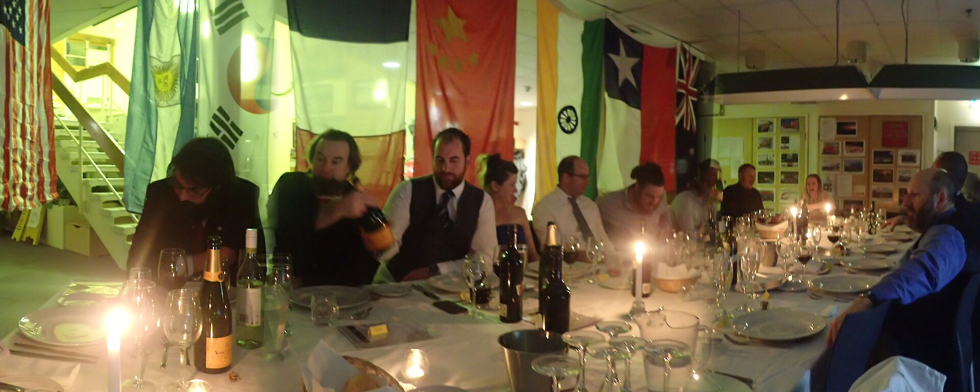 Midwinter dinner table with people sitting around it by candlelight.