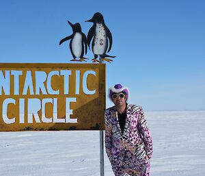 Chris in purple suit at the Antarctic Circle sign