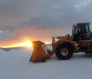 Dozer in front of winter sun on horizon.