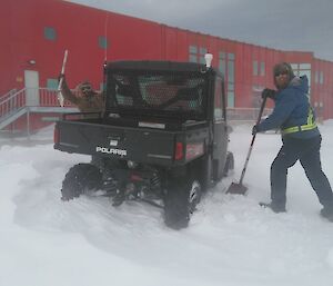 Two expeditioners digging out a bogged polaris vehicle