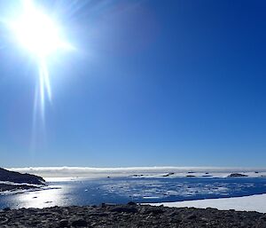 Sun in sky overlooking the ocean.