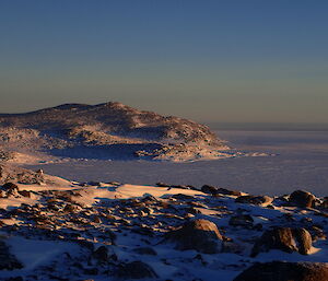 Snow covered hills looking over the ocean covered in ice.