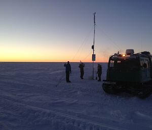 Expeditioners standing near a Hägg and the automatic weather station.