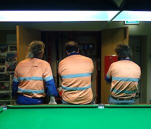 Three expeditioners watching a cupboard with a pump in it