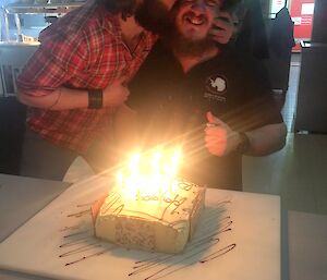 An expeditioner sitting at the table with a birthday cake gets a kiss from another expeditioner on the cheek.