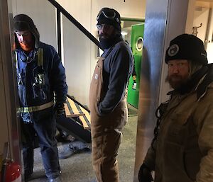 Three men stand inside looking at the building ready to make repairs.