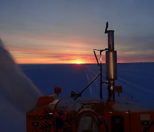 A view from the cab of the machinery blowing snow off the runway at sunset.