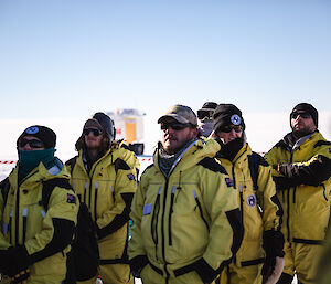 Personnel in outside Antarctic clothing standing outside in a group, listening to a briefing.