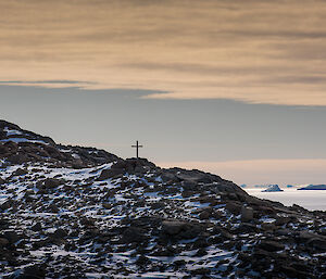 Stoney Hill in foreground with cross and two people silouetted against a sunset