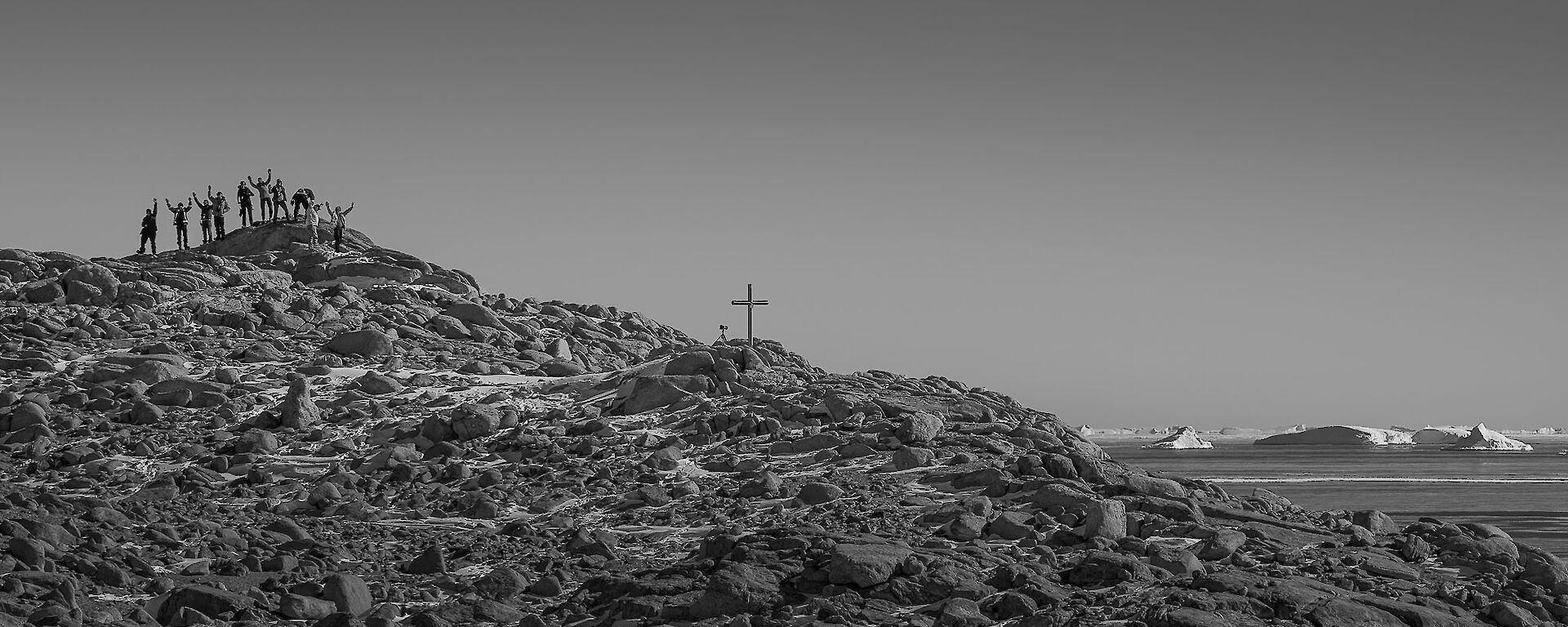 Rocky hill with cross on top with expeditioners sillouetted against the horizen