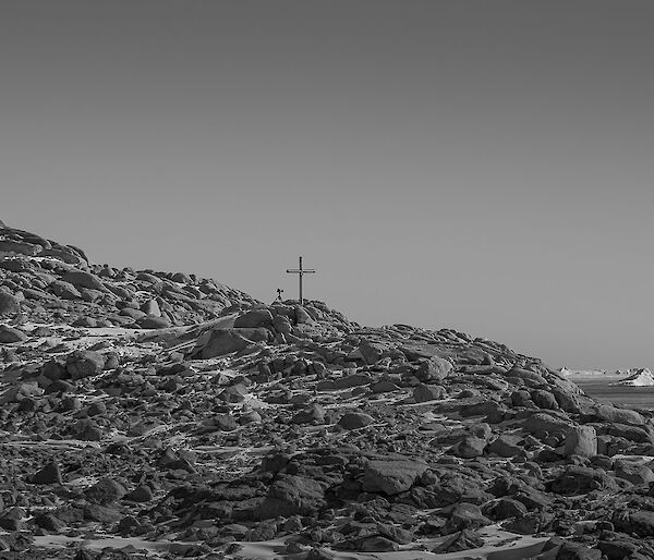 Rocky hill with cross on top with expeditioners sillouetted against the horizen