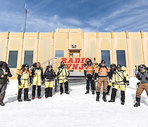A group of ten expeditioners wearing packs in front of Casey Operations Building