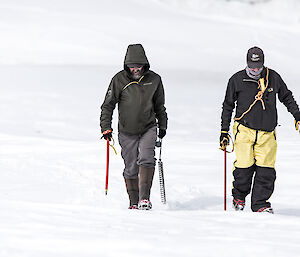 Two expeditioners carrying ice axes walking up icy hill