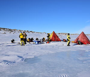 Field camp set up on ice and snow, Two red polar tens with expeditioners preparing field kitchen in mid-ground.