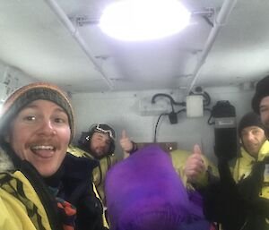 White painted inside of back cab of Hägglunds with four expeditioners smiling and relieved to be heading home, two giving thumbs up signal.