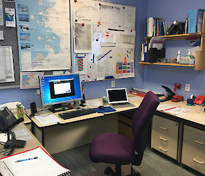 Office space with desks on three sides, Centre desk has computer screen and maps and whiteboard above.