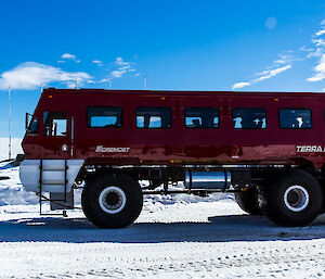 Large red bus with 1.5m high wheels, in foreground. In left background, casey sign with tags showing distance to Australian towns.