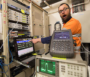 Man in high vis looking surprised and pointing at a compute screen in a computer rack.