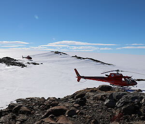 A helicopter on a pile of rocks with snow covered hills in the background.