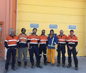 seven men standing in front of a big yellow roller door.