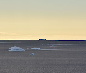 Grey sea with bergy bits floating in mid picture. At sunset, so sky is pale yellow.