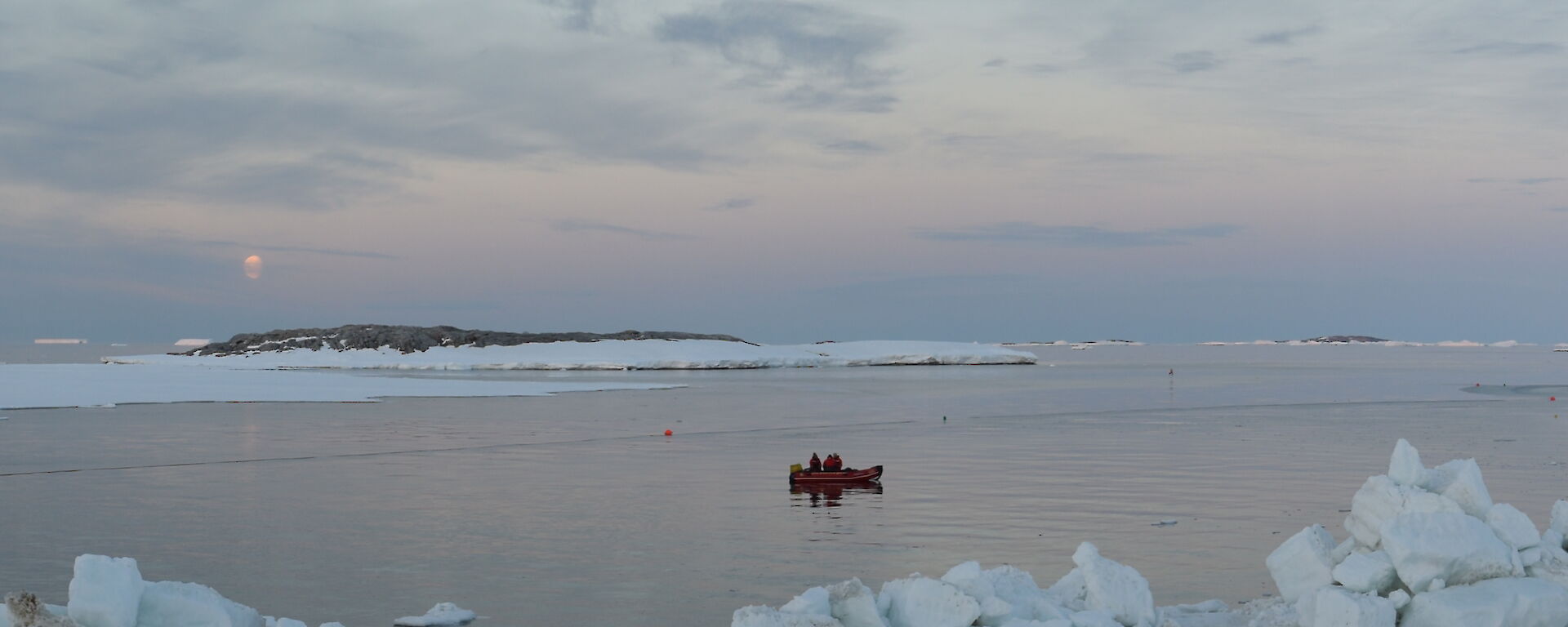 Wide shot of bay with snowy foreground and snow and rocky edge of bay in distance. Small red inflatable boat in centre picture