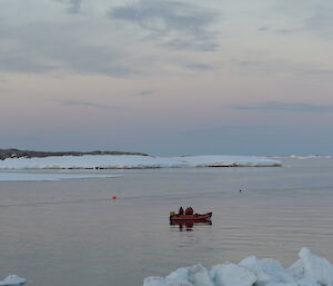 Wide shot of bay with snowy foreground and snow and rocky edge of bay in distance. Small red inflatable boat in centre picture