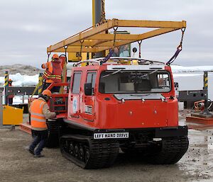 Red hagglands centre picture with yellow lifting frame above, Workmen in high vis jackets on the hagglunds detaching the frame.