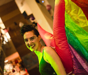 Woman smiling, wearing black singlet top and rainbow coloured wings