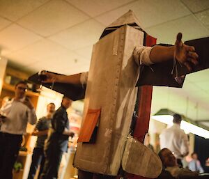 Man wearing cardboard costume of a fixed wing aircraft. People in background watching and taking photos