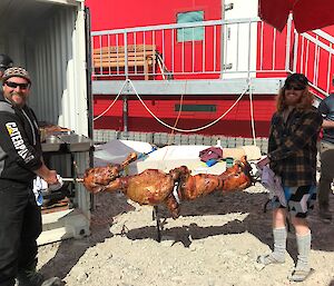 Men holding a spit with roast lamb and pig