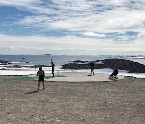 Three men playing cricket with backdrop of blue seas, icebergs and blue cloudy sky