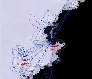 An aerial view of East Antarctica with a series of blue lines across the coastline showing flight routes. Mid picture is Casey Station, top right is the Shackleton Iceshelf, then left bottom third is Totten Glacier