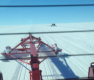 View from the rear of the tractor across the groomer to the snow runway into the distance. Blue sky above and second groomer in the distance.