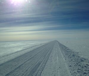White expanse with graded road projecting off into the distance. Blue cloud swept sky above.