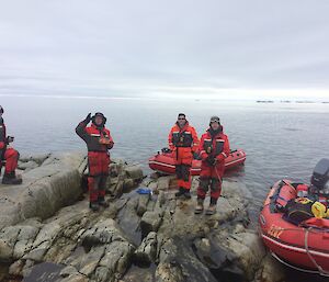 Boats pulled up to rocky shoreline with four people in red and black mustang suits hold the boat’s lines