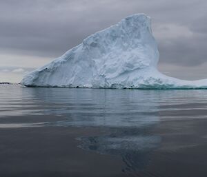 Grey water and skies with odd shaped iceberg with boat beside