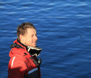 Man from shoulders up with mustang suit and goggles around neck. Blue sea behind