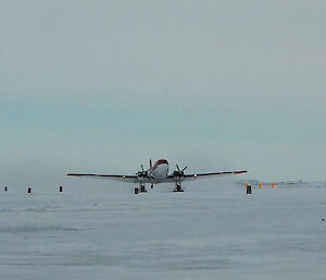 Ice runway with flag markers running along, Red and white plane on skis taxiing.