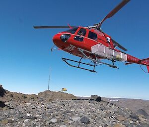 Rocky foreground with red helicopter hovering above and blue sky in background
