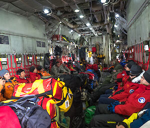 Inside of hercules aircraft with passengers sitting in hammock seating down either side and baggage in foreground