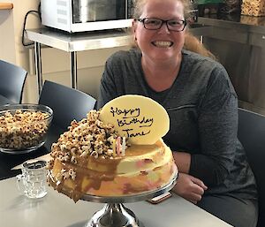 A lady sits behind a cake with popcorn on the top.