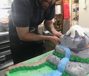 Chef stands over multilayered cake which is decorate to look like a snow capped mountain with a stream running off it