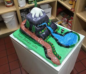 Inside the pantry, cake made to look like a snow capped mountain with stream and road running off it, on green base with ice flowers and trees