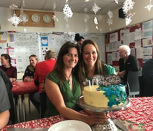 Two ladies sitting behind cake on table