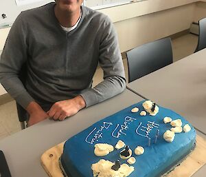 Man sitting at table with cake iced blue in front of him