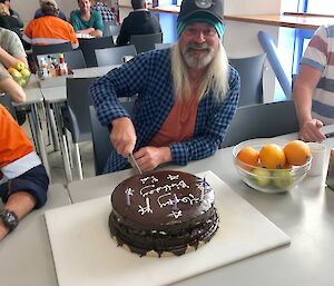 Man cutting into large round chocolate cake