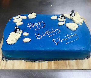 Cake on wooden board, iced in blue with decoration depicting icebergs and penguins