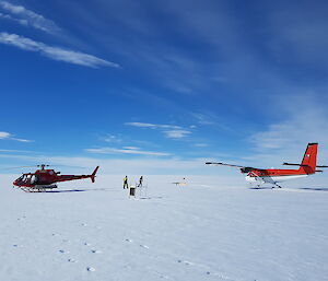Icy foreground stretching to horizon, blue sky with some white ciro-stratus clouds covering 1/3 of sky. Mid picture red helicopter on left and red and white twin prop plane on right. In the middle of the two aircraft, two people working
