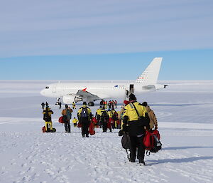 White A319 plane on apron of ice runway, Large group of expeditioners carrying carry on luggage heading down the slope towards the plane